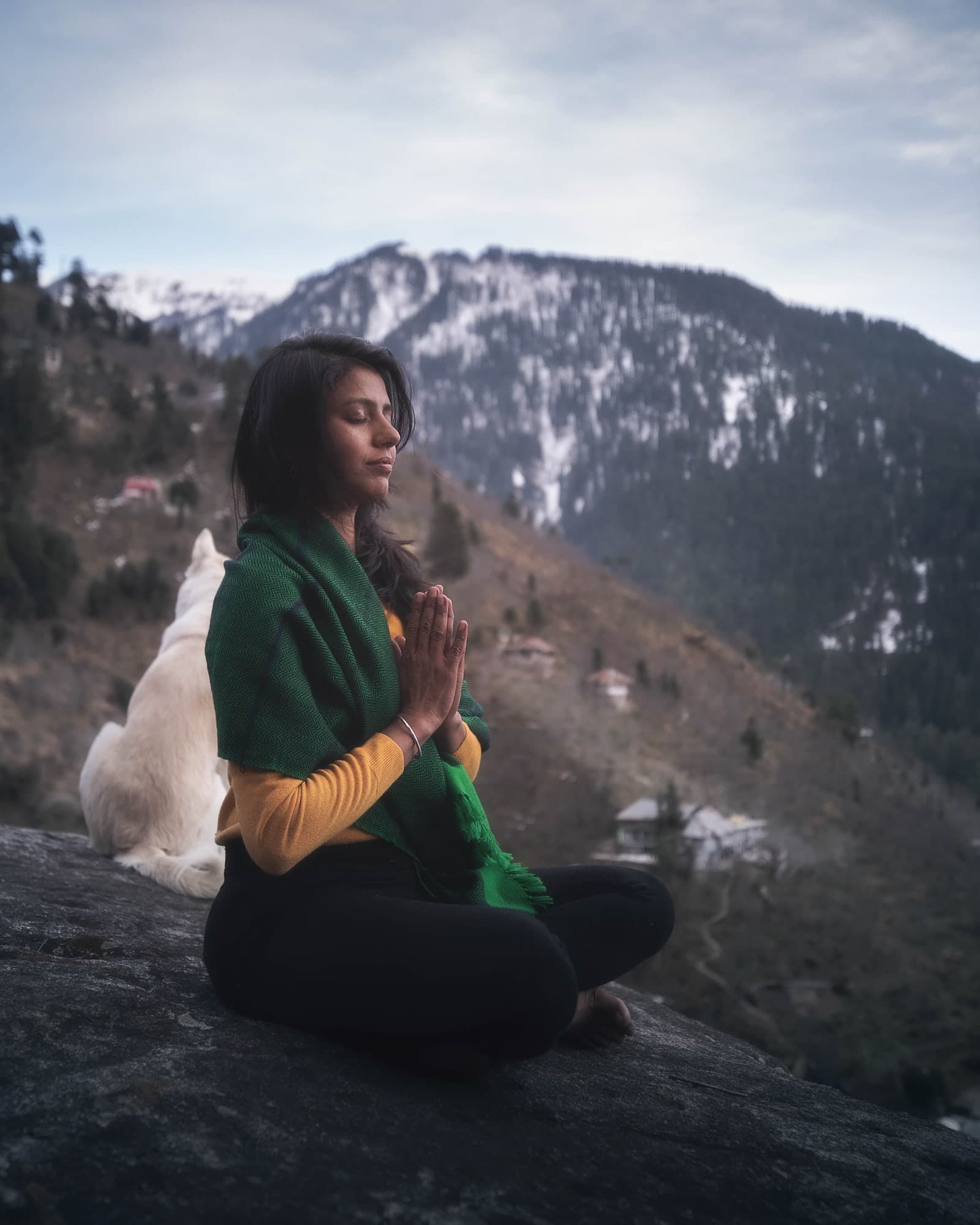Kavita meditating on a rock with snow-capped Himalayan peaks behind her