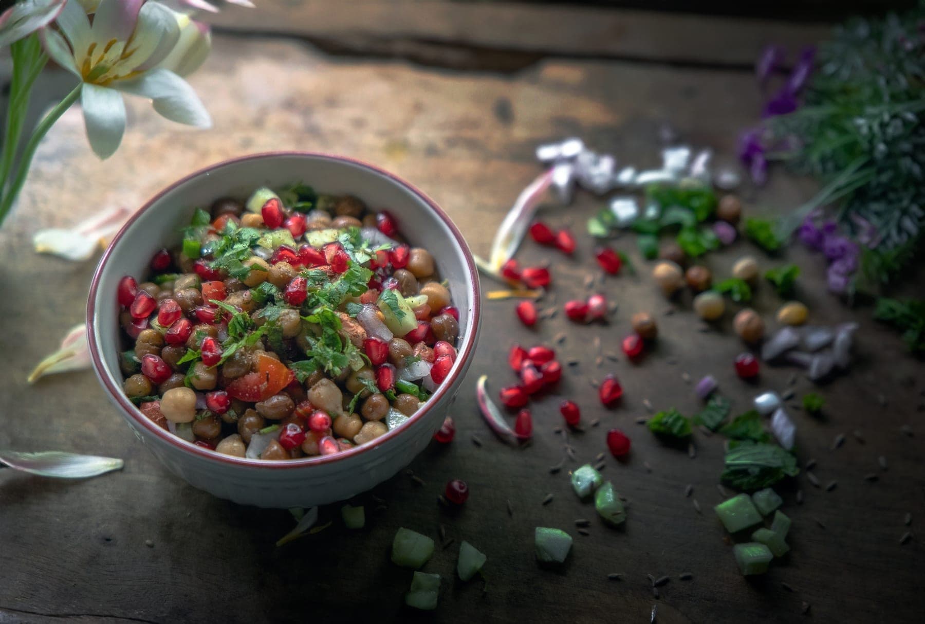 A fresh chickpea and pomegranate salad in a ceramic bowl on a wooden kitchen table